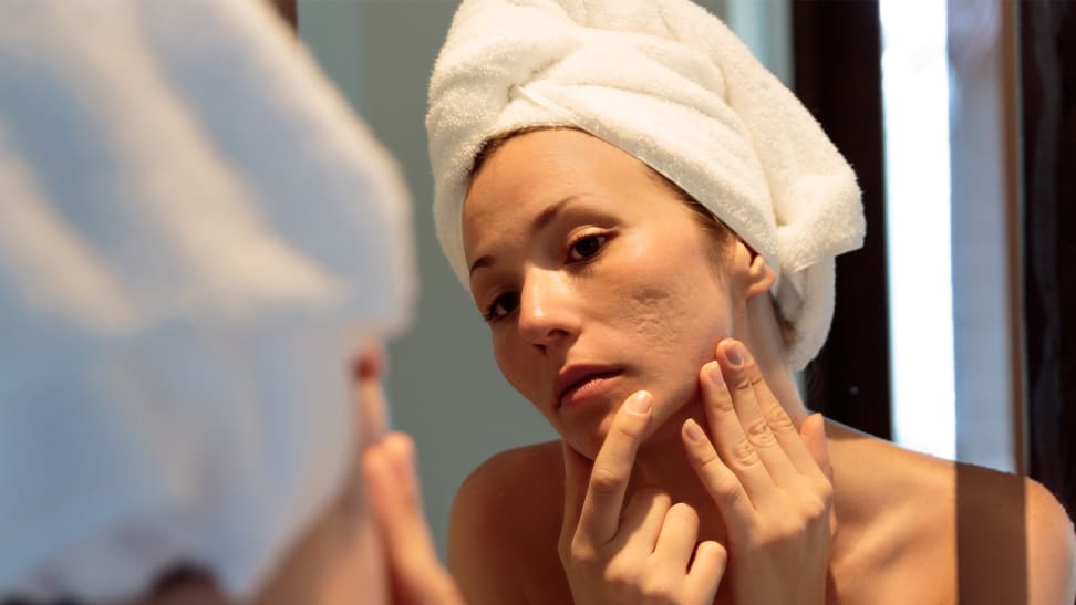 A woman looking into a mirror and holding her face while examining her acne scarring.