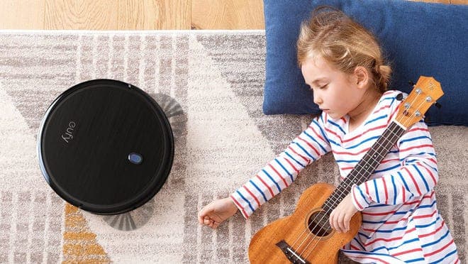 Girl resting on carpet next to sleek black robot vacuum