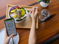 Person eating a hearty salad filled with colorful vegetables while tracking the calories through a diet app on a smartphone.