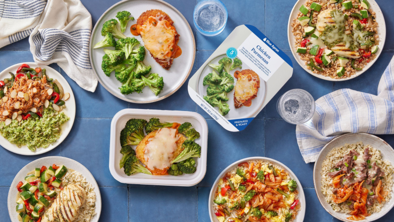 Several Blue Apron prepared meals in boxes and plated on a blue table