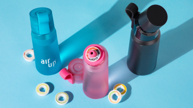Blue, pink, and black Air Up bottles surrounded by flavor pods on blue background