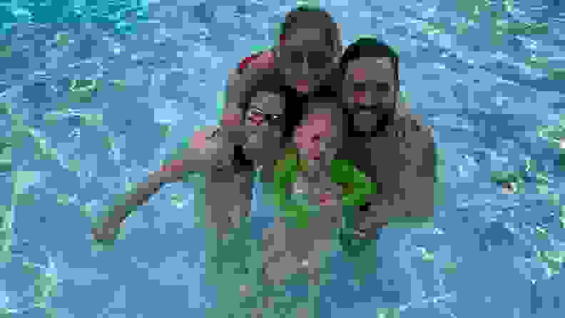 A family of four smiles together in a swimming pool.