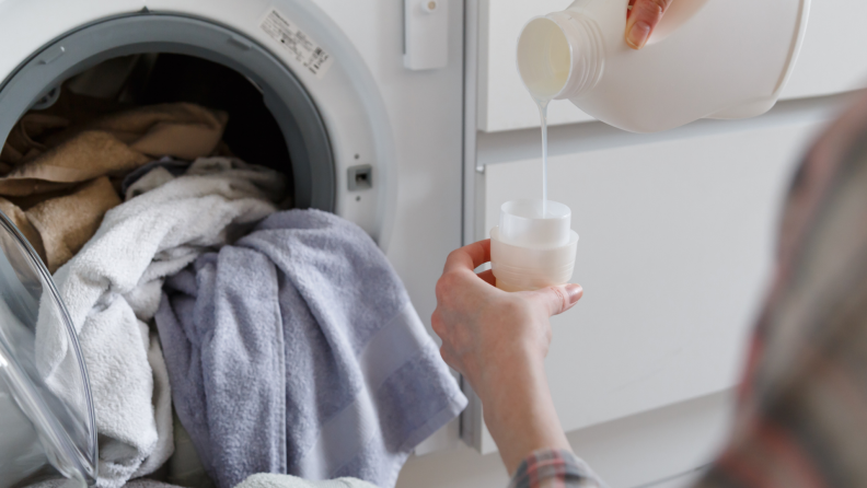 Closeup of a person pouring liquid laundry detergent into a cap while washing towels.