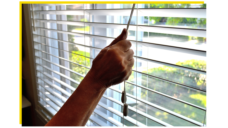 A hand closing some window blinds.