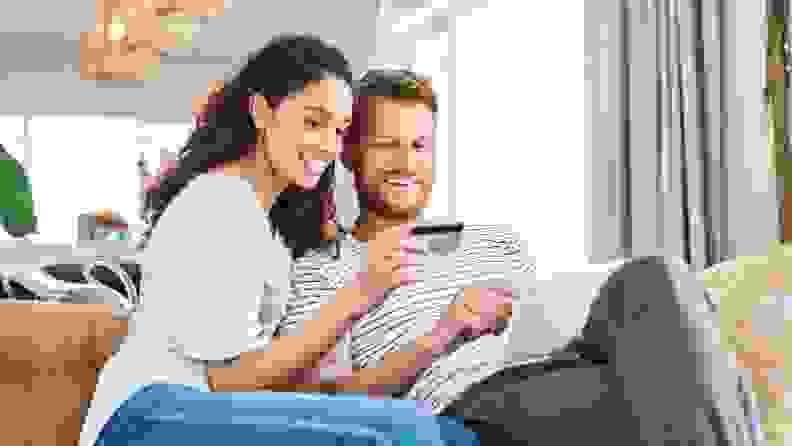 A couple sits on a couch as they look at a computer screen and hold up a credit card