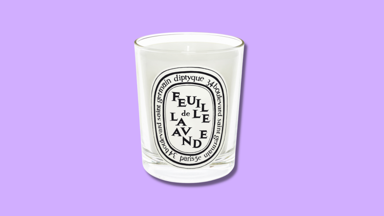 A Diptyque candle against a purple background.