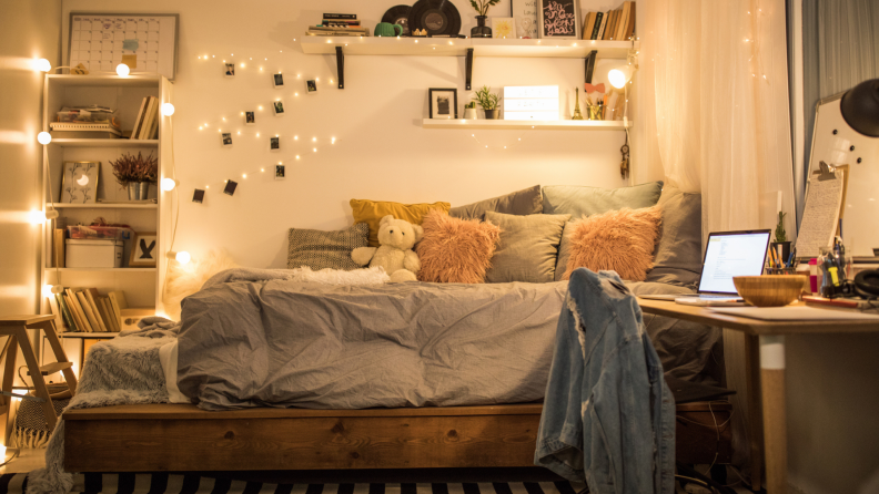 Teen bedroom with warm-colored string lights by the bed, curtains, and bookshelf