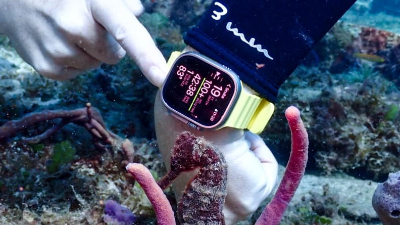 A diver skims along a coral reef as she checks the data on her Apple Watch Ultra.