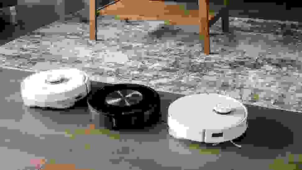 Three robot vacuum and mop hybrids lined up on a brown floor next to a rug.