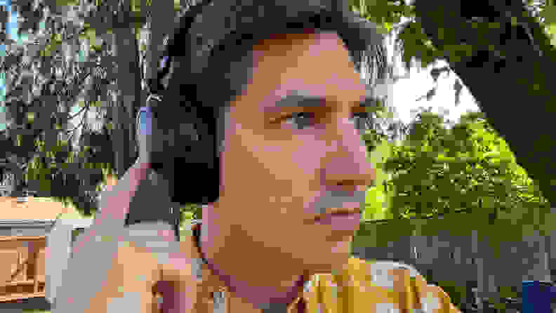 A man in a yellow pattern shirt uses the touch controls on a black pair of headphones in a green yard.