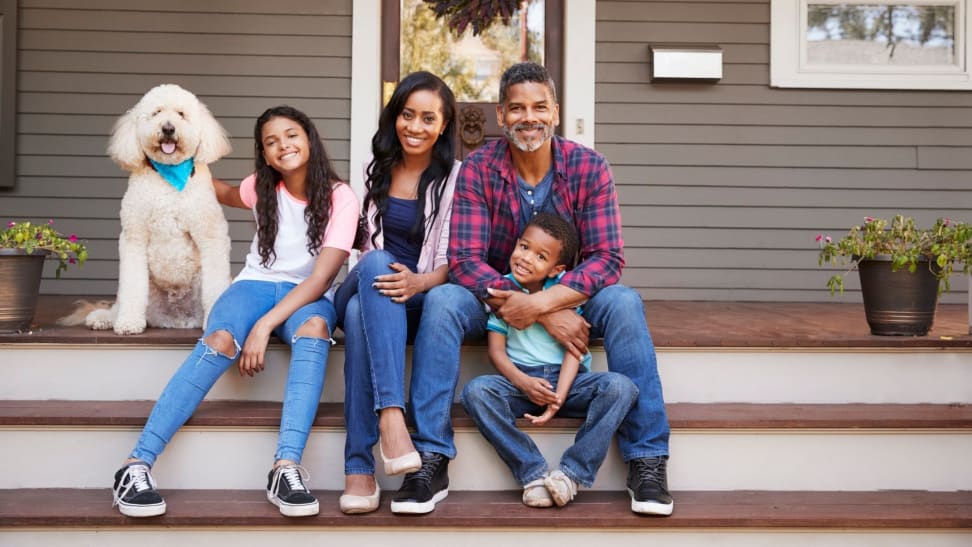 A family of four sits on the front steps of their home with their pet dog