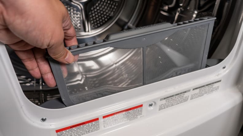 A close-up of a hand reaching into frame to remove the Frigidaire FFRE4120SW dryer's lint trap. It's about a third of the way removed in the photo.