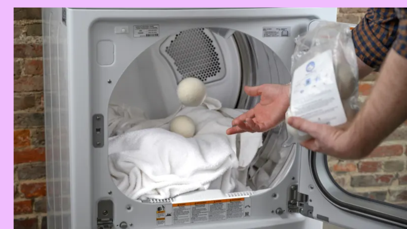 Person tossing in a wool dryer ball into a dryer with clean wet clothes