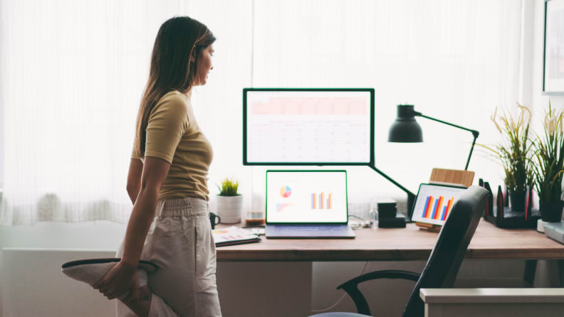A woman stretching her quad muscle standing at her desk.