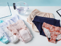 Six pairs of women's incontinence underwear from Speax, Knix, Always, Depend, and Wearever laying on a table with a measuring cup of water and a tray.
