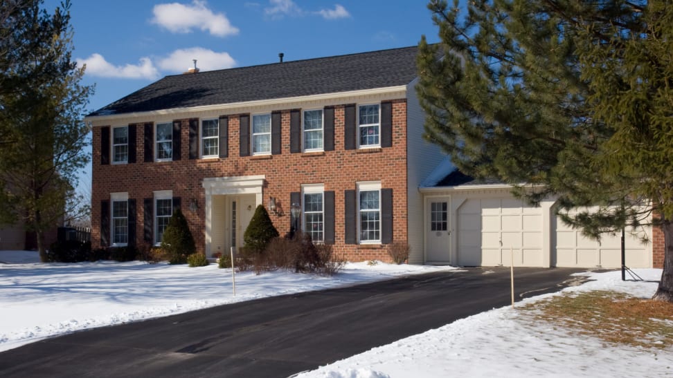 Two-story brick home with an attached garage and asphalt driveway with snow on the ground