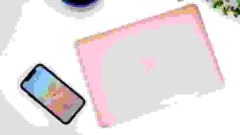 A pink MacBook Air and a smartphone on a white table viewed from above.