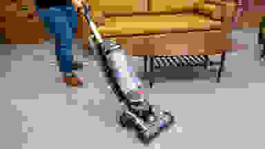 A person pushes the Hoover Swivel XL Pet upright vacuum across tan carpeting