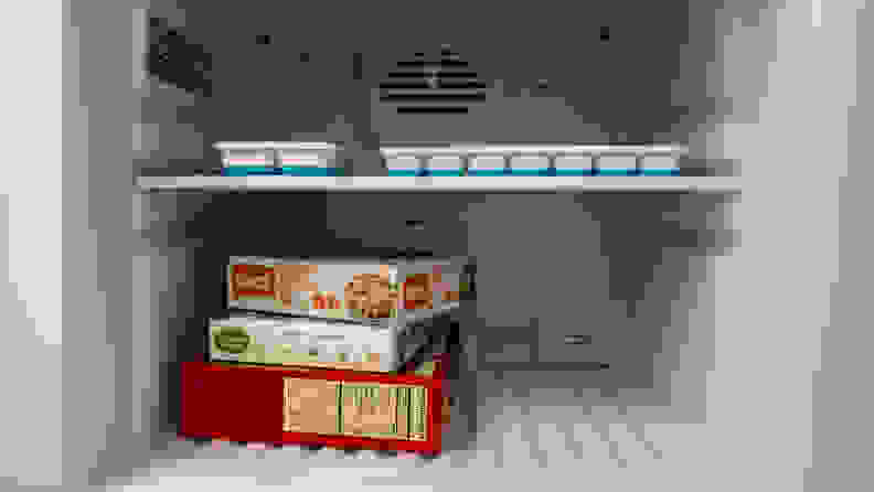 A close-up of the freezer compartment, with a few boxes of frozen food added for scale. A frozen pizza box takes up the entire width of the freezer.