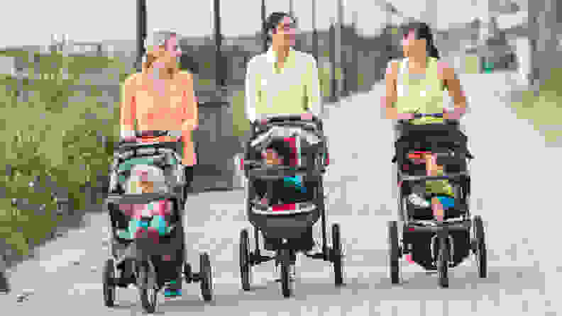 A group of three multi-ethnic mothers walking together, pushing their children in jogging strollers.  The child on the left, a 22 month old toddler with blond hair, is the oldest.  The African American girl and Asian boy are 11 months old.