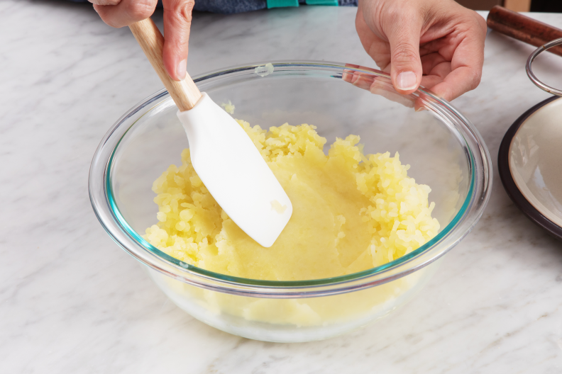 A hand using a spatula to spread across a batch of mashed potatoes