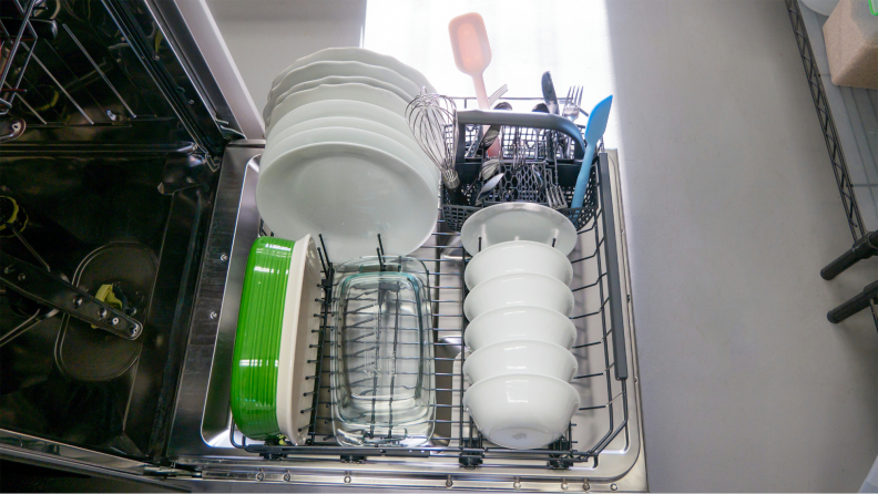 The Asko DBI564IXXLS Dishwasher’s lower rack is fully loaded with two baking pans, bowls, plates, and cutlery.