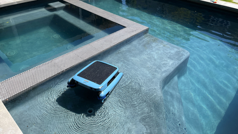 A square blue and black robot skimmer floats across a pool's surface