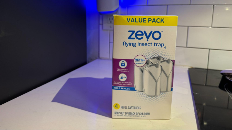 A box of a four-pack of Zevo Fly Trap refill cartridgges sitting on a white kitchen counter.