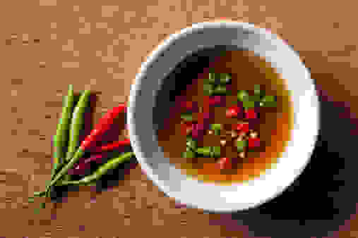 Chopped fiery hot Thai fresh red and green chili in a bowl of fish sauce on a cutting board. This type of chili is a major ingredient of Thai cuisine and is also used chopped up mixed with fish sauce as a complement with Thai food. In Thailand this small chili is called 'Phrik Kee Noo' and sometimes referred to as 'Birds Eye' chili. The salty fish sauce and chili traditional condiment is used to compliment most Thai dishes and in Thailand it is called 'Phrik Nam Pla'. You will find it on the table at all Thai restaurants in Thailand and is used by Thai's to sprinkle on their meal instead of salt.