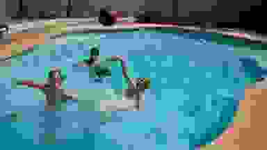 Three youths play pool basketball in an in-ground swimming pool.