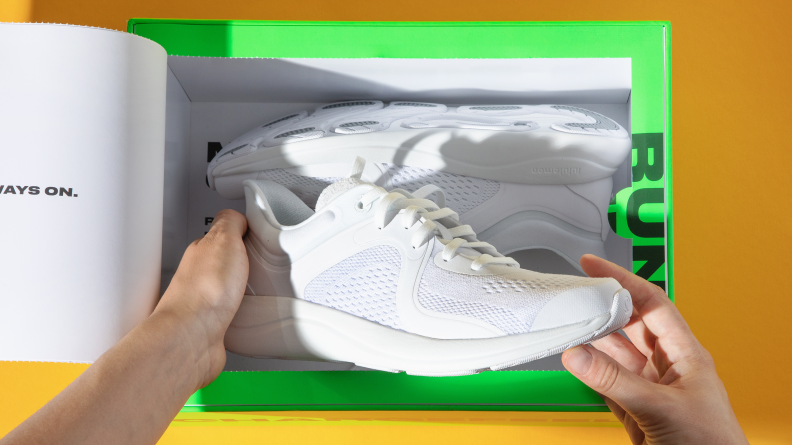 A pair of white Lululemon Chargefeel sneakers being pulled out of a neongreen box
