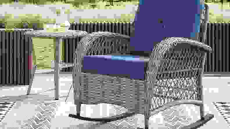 Wicker rocking chair with blue seat cushions outdoors.