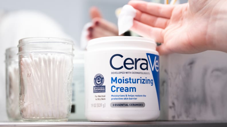 A hand dipping into a tub of moisturizer.
