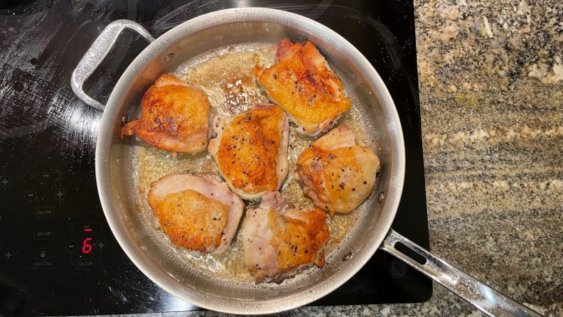 Six chicken thighs cooking in a stainless-steel pan.