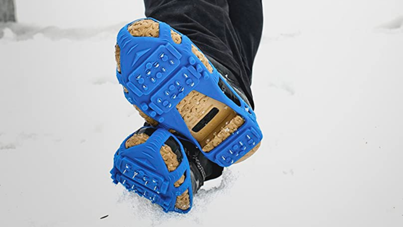 A person crosses their feet together in the snow wearing cleats.