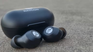 A pair of black earbuds with white highlights sit on grey pavement.