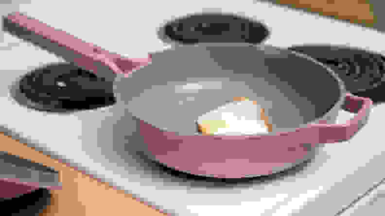 A lavender colored Always Pan is on a white stovetop with a fried egg in it.