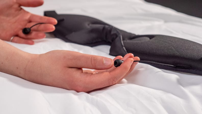 A person holds a pair of headphones in bed.