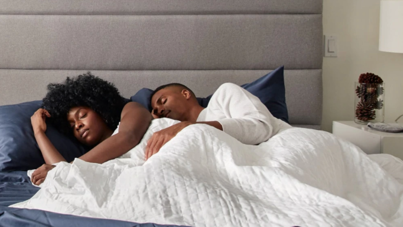 Couple sleeping together in bed under white weighted blanket.