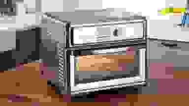 The Cuisinart Digital Air Fry Oven on a wood counter with french fries inside.