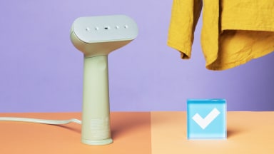 The Steamery Cirrus 3 standing upright on a table next to the Reviewed checkmark with a linen shirt in the background.