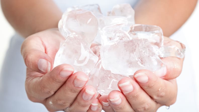 A person holds a heap of ice cubes in their cupped hands.