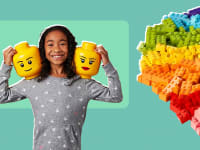 A girl holding two Lego heads on her shoulders next to a rainbow-colored pile of Legos.