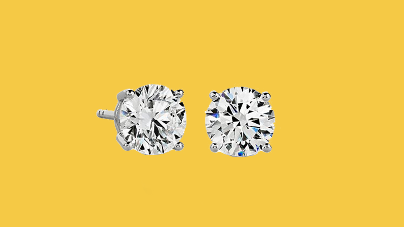 A pair of Blue Nile diamond stud earrings on a yellow background.