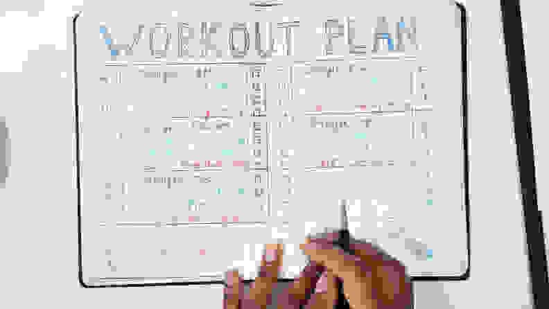 An Elevated View Of A Person Making Note Of Workout Plan On Notebook
