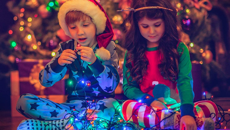 Two children play with colorful Christmas lights.