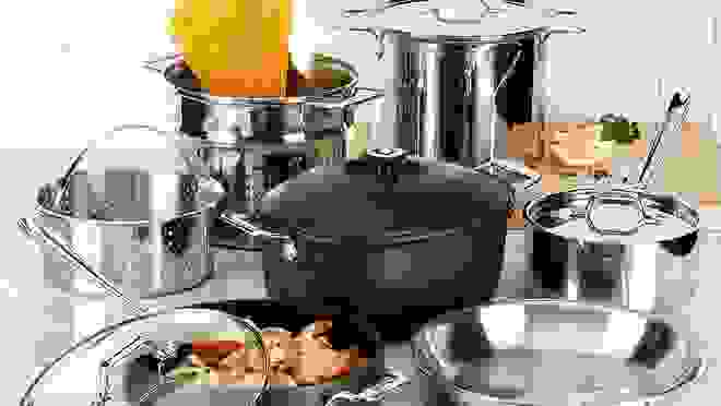 Assorted black and silver cookware set on kitchen countertop with raw pasta and cooked shrimp inside.