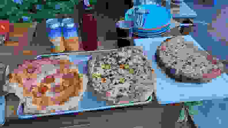 Three pizzas sit on a counter outdoors.