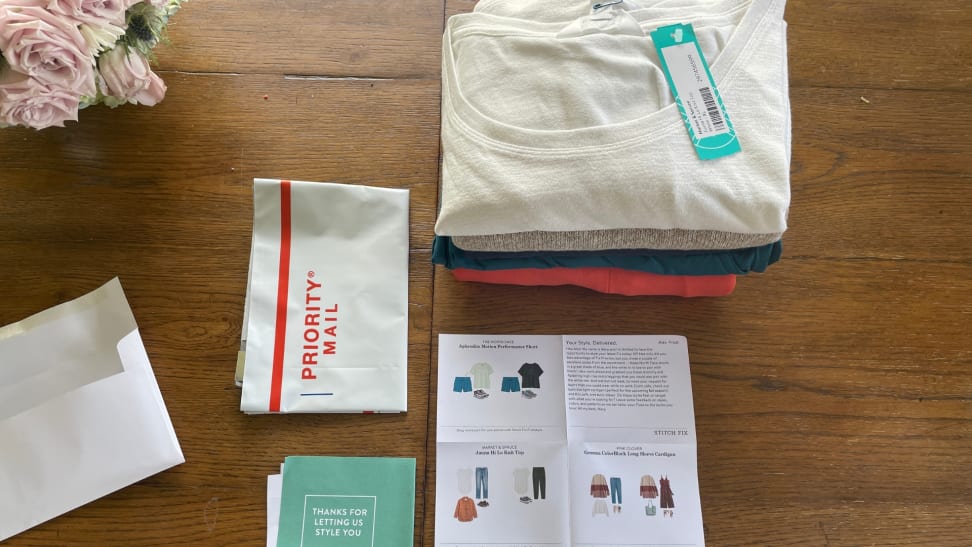 A folded stack of clothing next to a USPS envelope and welcome package instruction sheet from Stitch Fix.