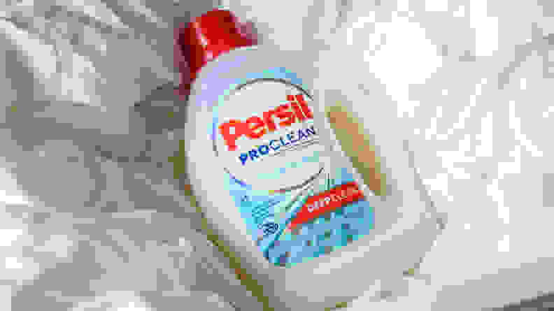 A bottle of Persil laundry detergent lays on top of white bedding